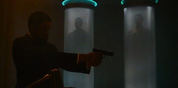 Movie still from “They Cloned Tyrone” (2023), directed by Juel Taylor – A man holding a gun in front of a wall; Medium shot, Over the shoulder angle