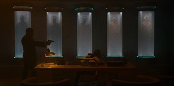 Movie still from “They Cloned Tyrone” (2023), directed by Juel Taylor – A person sitting at a table in front of a window; Wide shot, Low angle