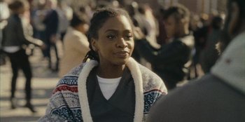 Movie still from “They Cloned Tyrone” (2023), directed by Juel Taylor – A woman in a crowd of people wearing a sweater; Close Up shot, Over the shoulder angle