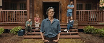 Movie still from “They/Them” (2022), directed by John Logan – A man standing in front of a group of people on a porch; Medium shot, Low angle
