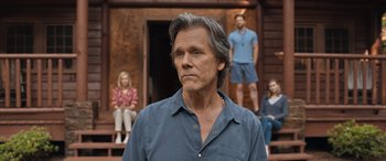 Movie still from “They/Them” (2022), directed by John Logan – A man standing in front of a group of people on a porch; Medium shot, Over the shoulder angle