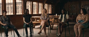 Movie still from “They/Them” (2022), directed by John Logan – A group of people sitting in a room with tables; Wide shot, High angle