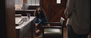 Movie still from “They/Them” (2022), directed by John Logan – A woman sitting on the floor in front of a desk; Medium shot, Over the shoulder angle