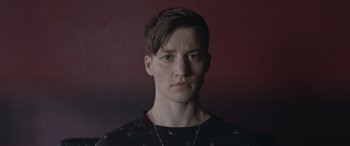 Movie still from “They/Them” (2022), directed by John Logan – A person with short hair is looking at the camera; Close Up shot, Low angle