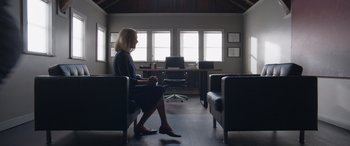 Movie still from “They/Them” (2022), directed by John Logan – A woman sitting on a chair in a room; Wide shot, Low angle