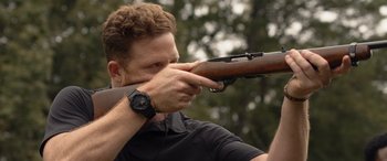 Movie still from “They/Them” (2022), directed by John Logan – A man holding a rifle while wearing a watch; Close Up shot, Over the shoulder angle