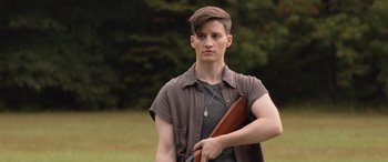 Movie still from “They/Them” (2022), directed by John Logan – A young man holding a gun in a field; Medium shot, Over the shoulder angle