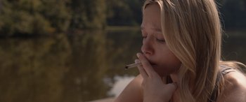 Movie still from “They/Them” (2022), directed by John Logan – A woman is smoking a cigarette near a body of water; Close Up shot, High angle