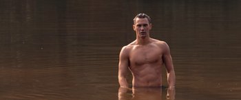 Movie still from “They/Them” (2022), directed by John Logan – A man standing in a body of water with no shirt on; Medium shot, High angle