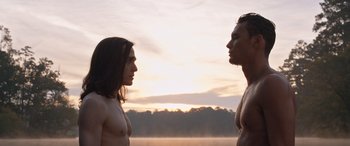 Movie still from “They/Them” (2022), directed by John Logan – A man and a woman standing next to each other in front of a sunset; Medium shot, Low angle