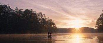 Movie still from “They/Them” (2022), directed by John Logan – A person sitting in the middle of a body of water at sunset; Extreme Wide shot, Low angle