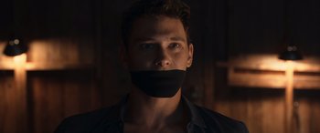 Movie still from “They/Them” (2022), directed by John Logan – A man with a black duct taped to his face; Close Up shot, Low angle