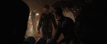 Movie still from “Thirteen Lives” (2022), directed by Ron Howard – A group of people walking in the rain with umbrellas; Medium shot, Over the shoulder angle
