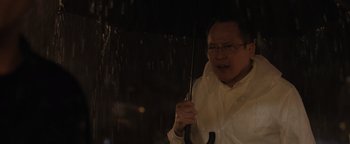 Movie still from “Thirteen Lives” (2022), directed by Ron Howard – An older man holding an umbrella in the rain; Close Up shot, Low angle