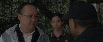 Movie still from “Thirteen Lives” (2022), directed by Ron Howard – A man and two women standing next to each other in front of bushes; Close Up shot, Over the shoulder angle