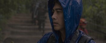 Movie still from “Thirteen Lives” (2022), directed by Ron Howard – A young man wearing a blue rain jacket; Close Up shot, Low angle