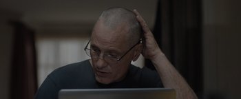 Movie still from “Thirteen Lives” (2022), directed by Ron Howard – A bald man with glasses is sitting at a computer; Close Up shot, Over the shoulder angle