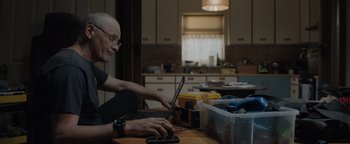 Movie still from “Thirteen Lives” (2022), directed by Ron Howard – A man sitting at a kitchen table using a laptop computer; Medium shot, Low angle