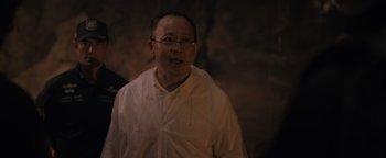 Movie still from “Thirteen Lives” (2022), directed by Ron Howard – An older man wearing glasses and a white shirt; Close Up shot, Over the shoulder angle