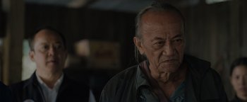 Movie still from “Thirteen Lives” (2022), directed by Ron Howard – An old man with long grey hair looking at the camera; Close Up shot, Over the shoulder angle