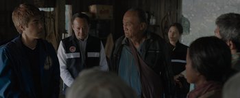 Movie still from “Thirteen Lives” (2022), directed by Ron Howard – Two men are standing in front of a group of people; Medium shot, Over the shoulder angle