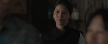 Movie still from “Thirteen Lives” (2022), directed by Ron Howard – A woman in a black jacket is looking at the camera; Close Up shot, Over the shoulder angle