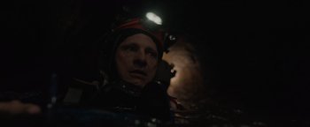 Movie still from “Thirteen Lives” (2022), directed by Ron Howard – A man with a helmet on his head in the dark; Close Up shot, Overhead angle