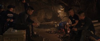 Movie still from “Thirteen Lives” (2022), directed by Ron Howard – Two men sitting on the ground in front of a cave; Wide shot, High angle