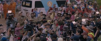 Movie still from “Thirteen Lives” (2022), directed by Ron Howard – A group of people standing around a crowd of people; Medium shot, Over the shoulder angle