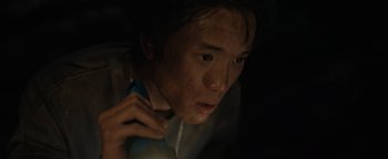 Movie still from “Thirteen Lives” (2022), directed by Ron Howard – A young man holding a cell phone up to his ear; Close Up shot, High angle
