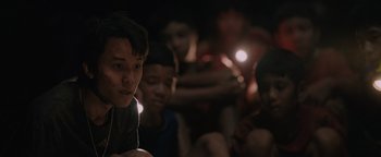 Movie still from “Thirteen Lives” (2022), directed by Ron Howard – A group of young people sitting in a dark room; Close Up shot, Over the shoulder angle