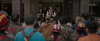 Movie still from “Thirteen Lives” (2022), directed by Ron Howard – A group of people standing in front of a building; Medium shot, Over the shoulder angle