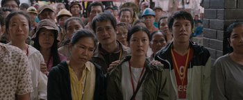 Movie still from “Thirteen Lives” (2022), directed by Ron Howard – A large group of people standing together in a crowd; Medium shot, High angle