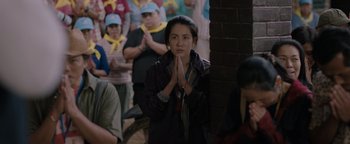 Movie still from “Thirteen Lives” (2022), directed by Ron Howard – A woman is praying in front of a group of people; Medium shot, Over the shoulder angle