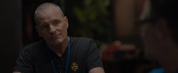 Movie still from “Thirteen Lives” (2022), directed by Ron Howard – A man with a bald head sitting in front of a tree; Close Up shot, Over the shoulder angle