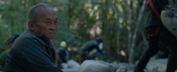 Movie still from “Thirteen Lives” (2022), directed by Ron Howard – An older man standing in front of a pile of garbage; Close Up shot, Over the shoulder angle
