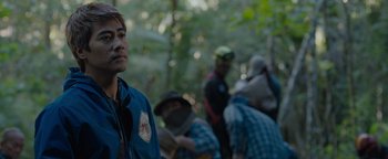 Movie still from “Thirteen Lives” (2022), directed by Ron Howard – A group of people standing in the woods near a forest; Close Up shot, Over the shoulder angle