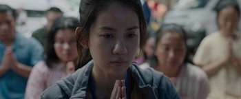 Movie still from “Thirteen Lives” (2022), directed by Ron Howard – A woman is praying in a crowd of people; Close Up shot, High angle