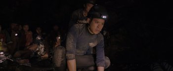 Movie still from “Thirteen Lives” (2022), directed by Ron Howard – A man with a helmet on sitting next to another man; Medium shot, High angle