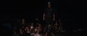 Movie still from “Thirteen Lives” (2022), directed by Ron Howard – A group of people sitting in the dark with lights on their heads; Wide shot, High angle