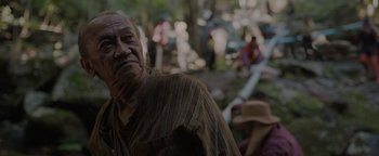 Movie still from “Thirteen Lives” (2022), directed by Ron Howard – An old man standing in the woods looking at the camera; Close Up shot, Over the shoulder angle