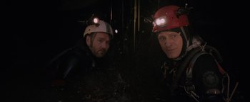 Movie still from “Thirteen Lives” (2022), directed by Ron Howard – Two men wearing hard hats and helmets in the dark; Medium shot, Overhead angle