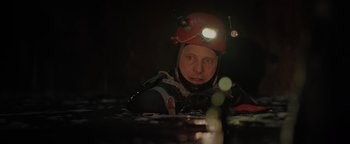 Movie still from “Thirteen Lives” (2022), directed by Ron Howard – A person wearing a helmet while sitting in a pool of water; Close Up shot, Over the shoulder angle