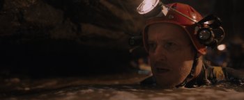 Movie still from “Thirteen Lives” (2022), directed by Ron Howard – A man with a helmet on his head looking into a cave; Close Up shot, High angle