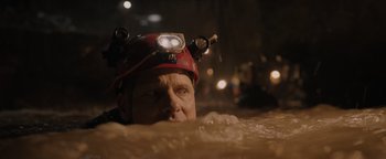 Movie still from “Thirteen Lives” (2022), directed by Ron Howard – A man wearing a hard hat in the middle of a river; Close Up shot, Over the shoulder angle