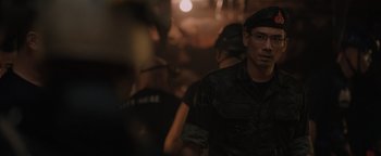 Movie still from “Thirteen Lives” (2022), directed by Ron Howard – A group of people standing in a room with lights in the background; Close Up shot, Over the shoulder angle