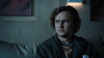 Movie still from “Escape Room” (2019), directed by Adam Robitel – A man sitting on top of a white couch looking at the camera; Close Up shot, Low angle