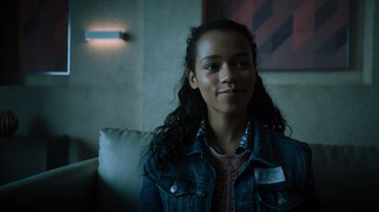 Movie still from “Escape Room” (2019), directed by Adam Robitel – A woman sitting on a couch in front of a painting; Close Up shot, Over the shoulder angle