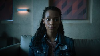 Movie still from “Escape Room” (2019), directed by Adam Robitel – A young woman sitting on top of a couch in front of a painting; Close Up shot, Over the shoulder angle