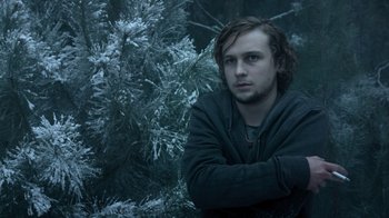 Movie still from “Escape Room” (2019), directed by Adam Robitel – A man standing in front of a tree in a wooded area; Medium shot, Low angle